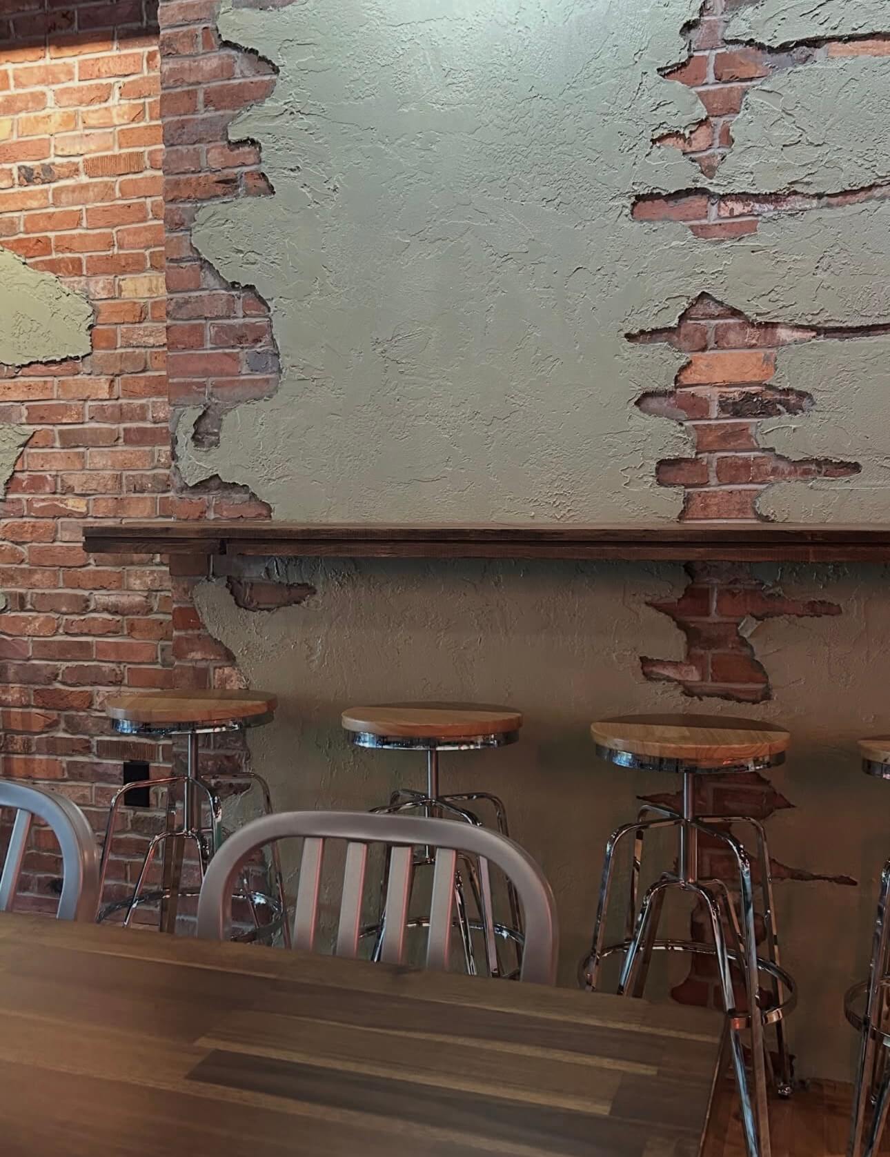 Stools tucked under the counter rail along the brick and sage plaster wall