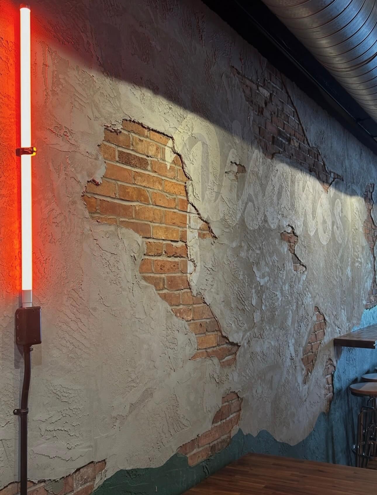 The Pisano&rsquo;s script painted across the plaster wall beside a red neon tube