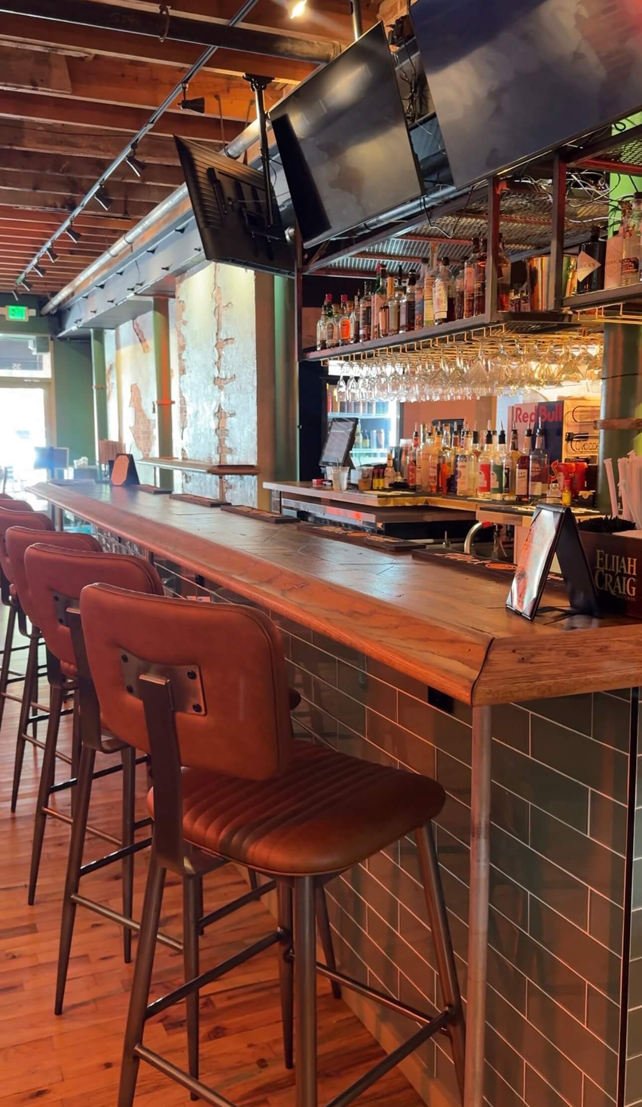 The bar with bottles on the shelves, glassware hanging overhead and televisions above the counter