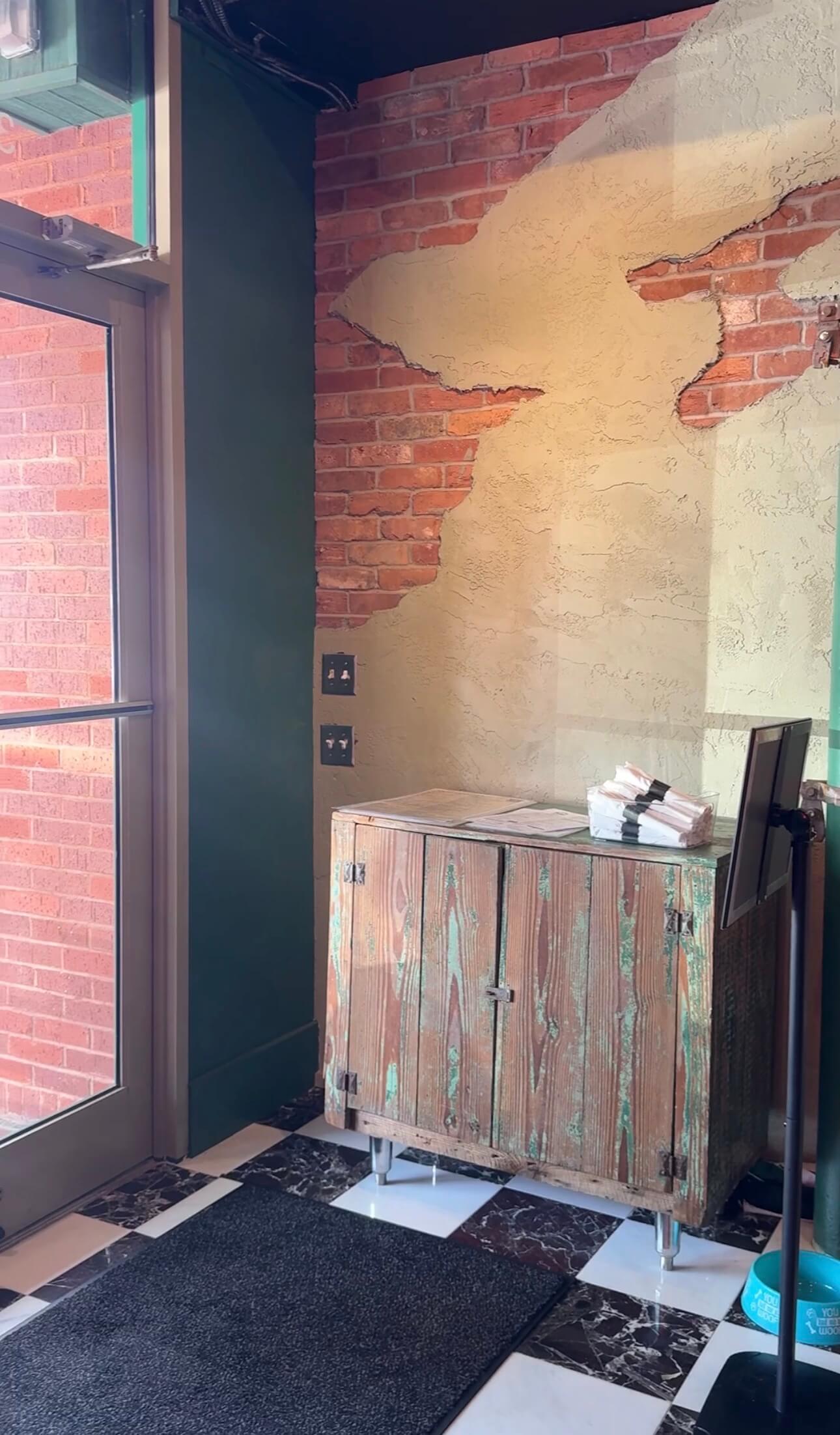The host stand inside the front door, on checkerboard tile against the brick and plaster wall